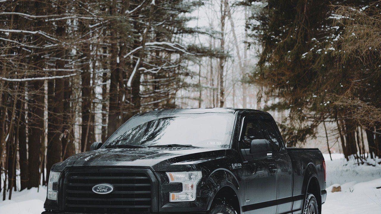Ford F-150 noir sur un chemin enneigé en forêt, illustrant les conditions hivernales québécoises qui augmentent le coût total de possession